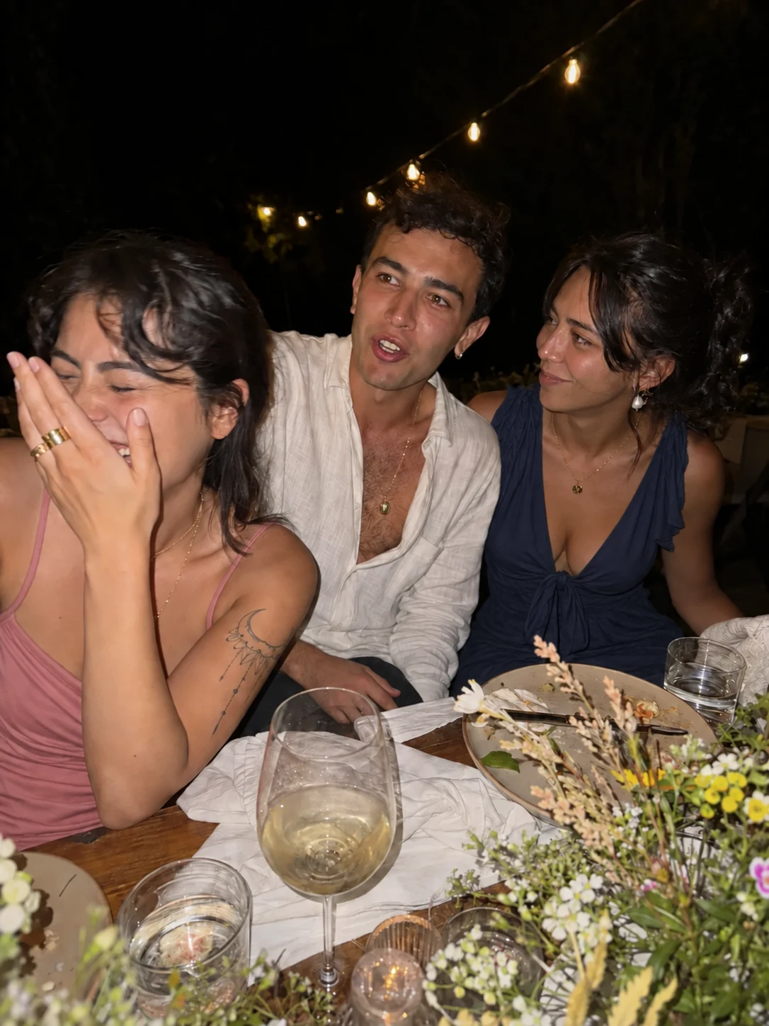 Friends laughing at a wedding table under string lights